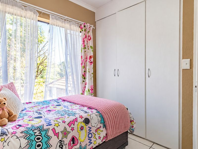 A bright bedroom featuring built-in cupboards, tiled flooring, and a large window allowing for natural light.