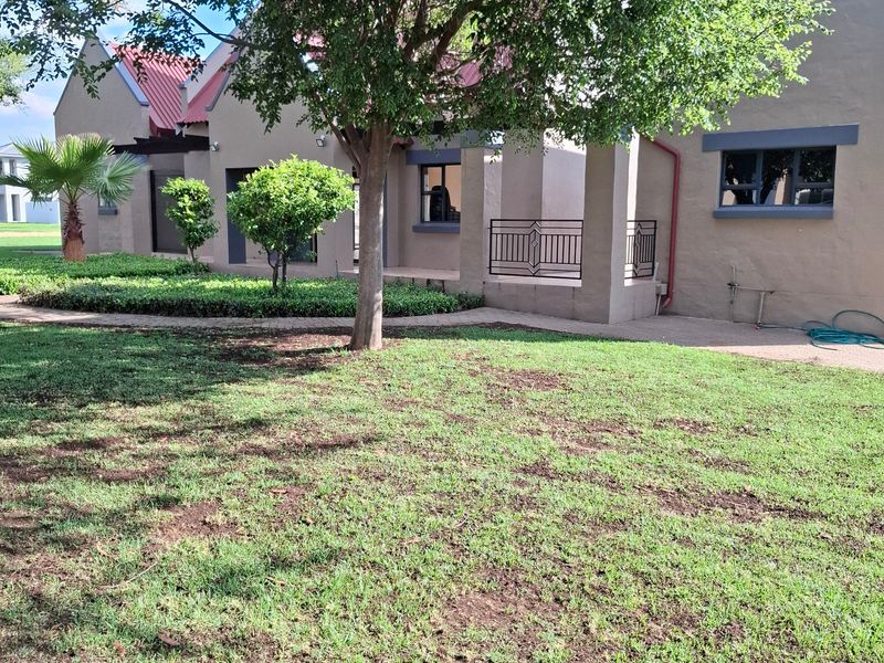 A view of the rear exterior of the property featuring a landscaped garden, paved walkway, and a metal roof structure.