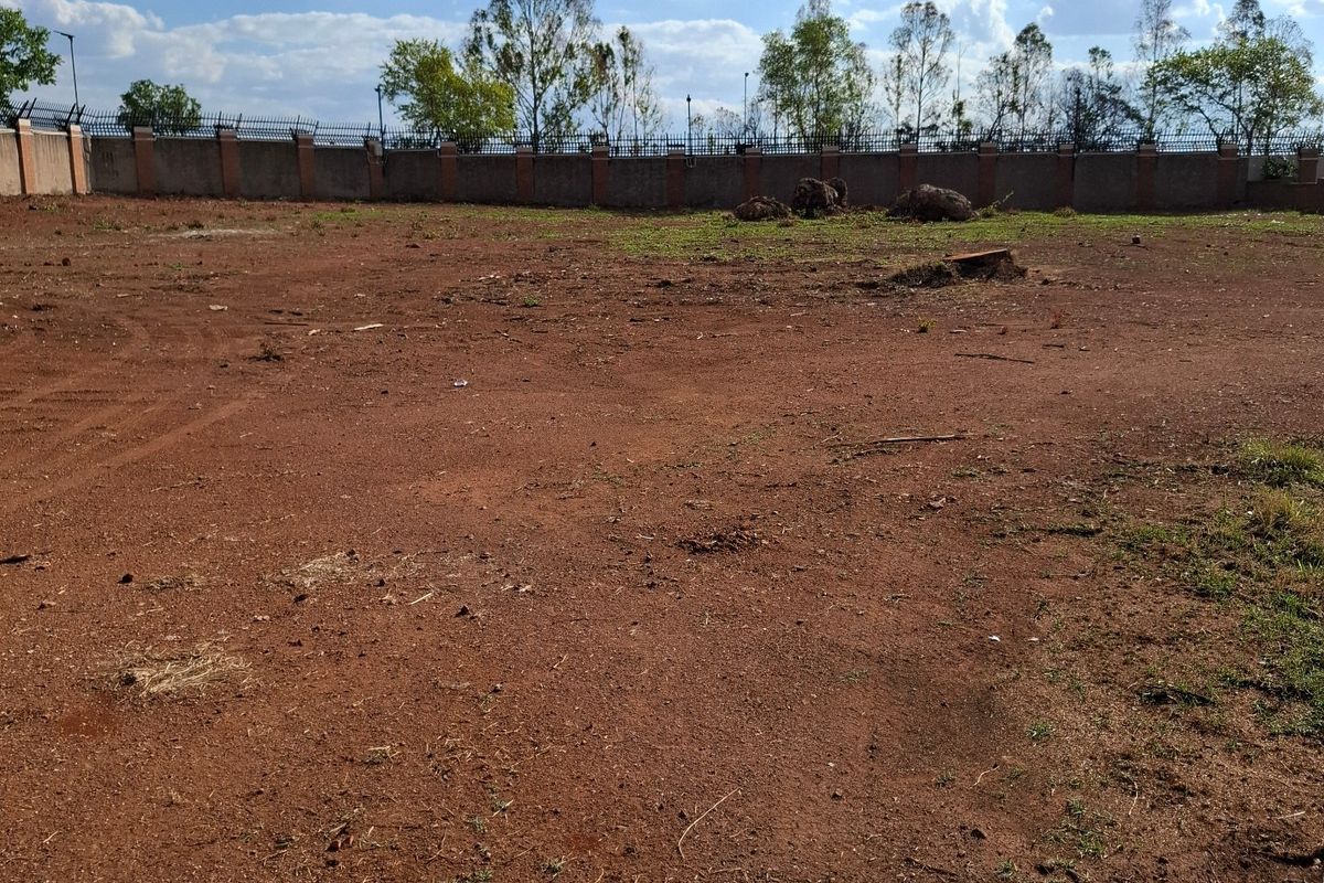 A vacant residential plot featuring cleared red earth and a secure perimeter wall with fencing along the boundary.