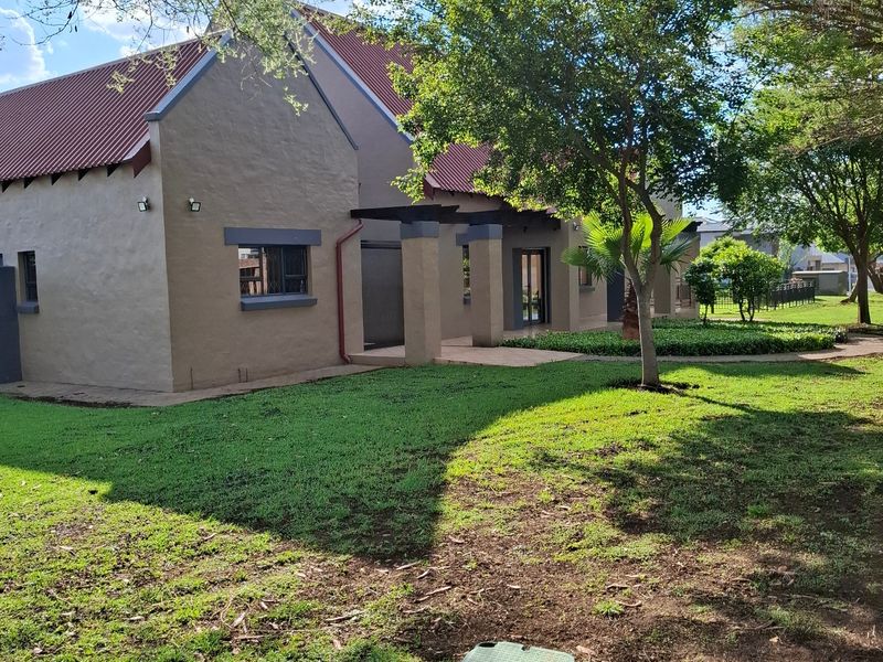 A well-maintained rear exterior view of the residence featuring a pitched roof, covered patio area, and established garden landscaping.