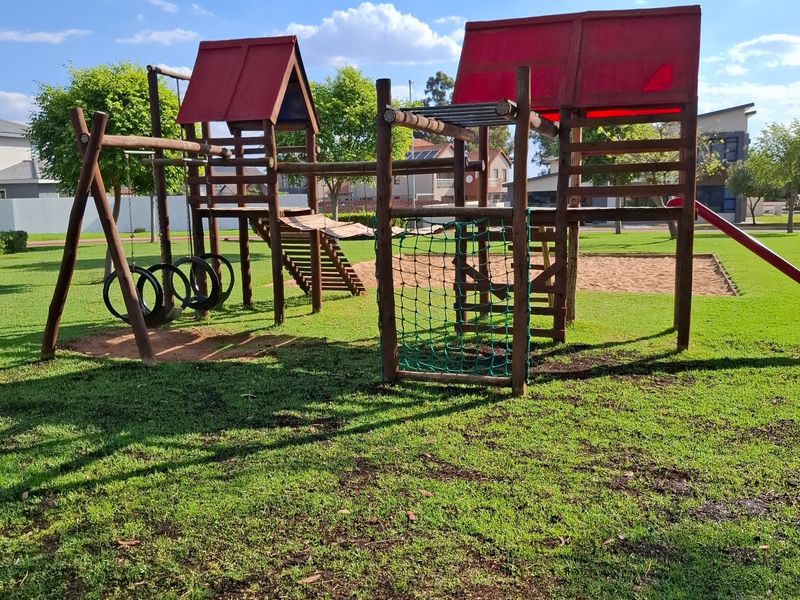 A well-maintained residential garden featuring a wooden playground structure with a sand pit and lush green lawn.
