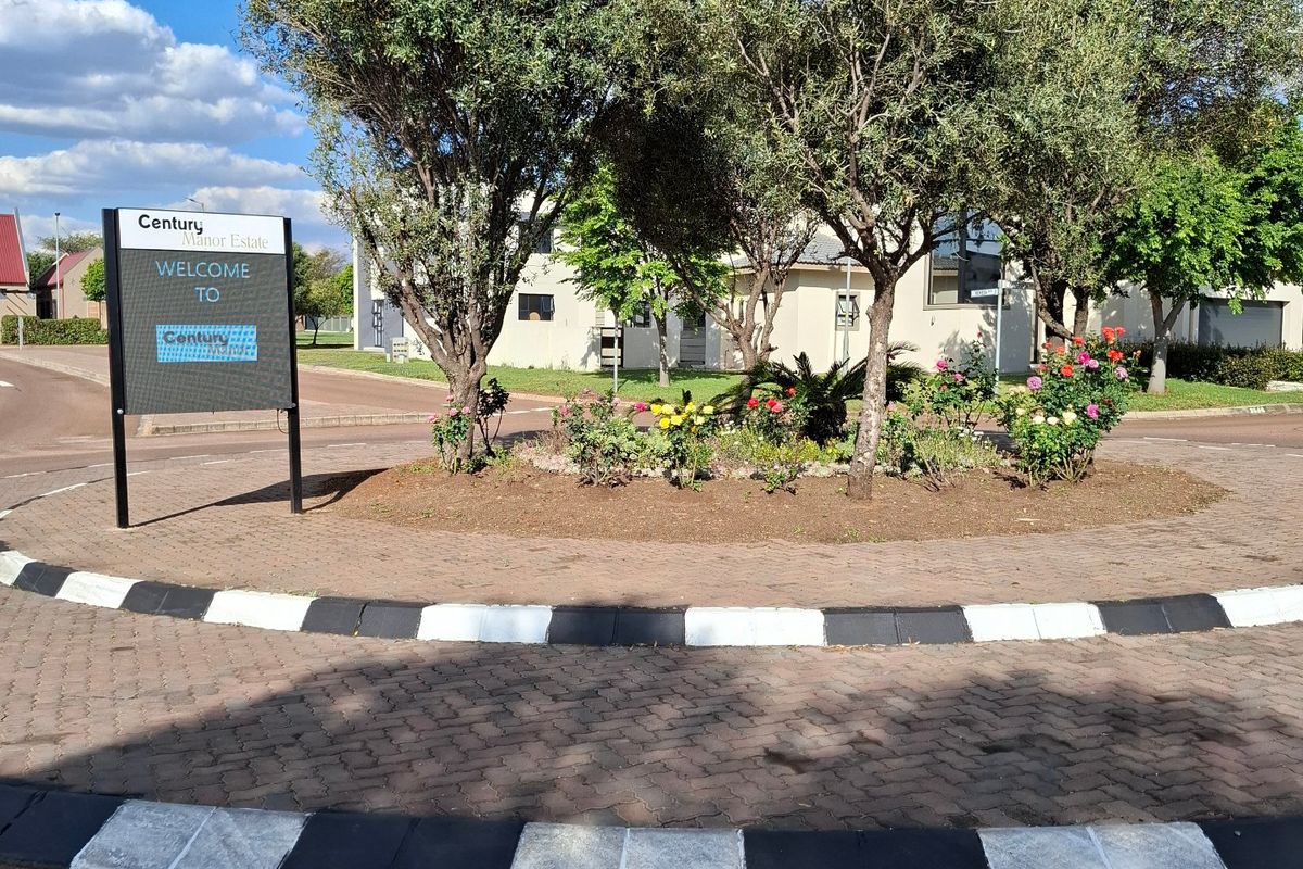 A view of the Century Manor Estate entrance featuring a paved roundabout, landscaped garden bed, and estate signage.