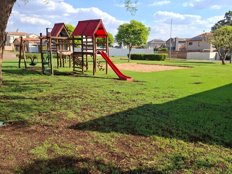 A well-maintained residential garden featuring a built-in playground structure with a slide and a sandpit area.