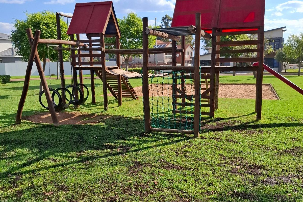 A well-maintained residential garden featuring a wooden playground structure with a sand pit and lush green lawn.