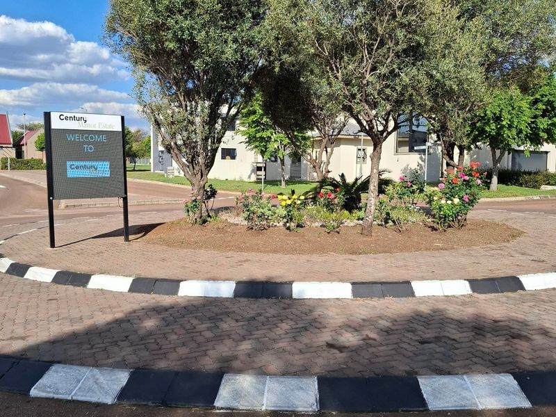 A view of the Century Manor Estate entrance featuring a paved roundabout, landscaped garden bed, and estate signage.