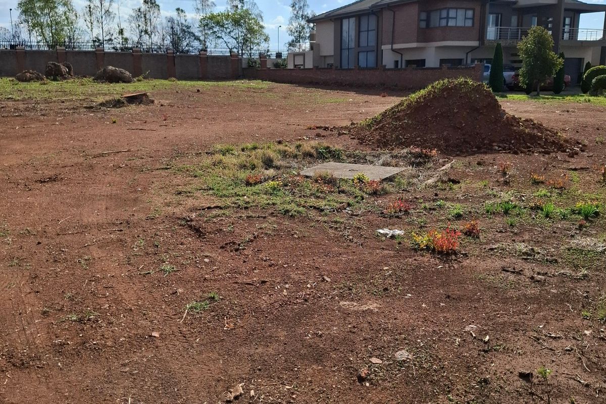 A vacant residential plot featuring cleared earth, a perimeter brick wall, and a central manhole cover, ready for development.