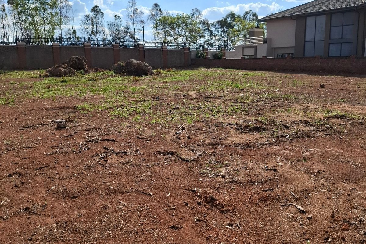 A vacant residential plot featuring red soil, perimeter walling, and security fencing, offering a blank canvas for future development.