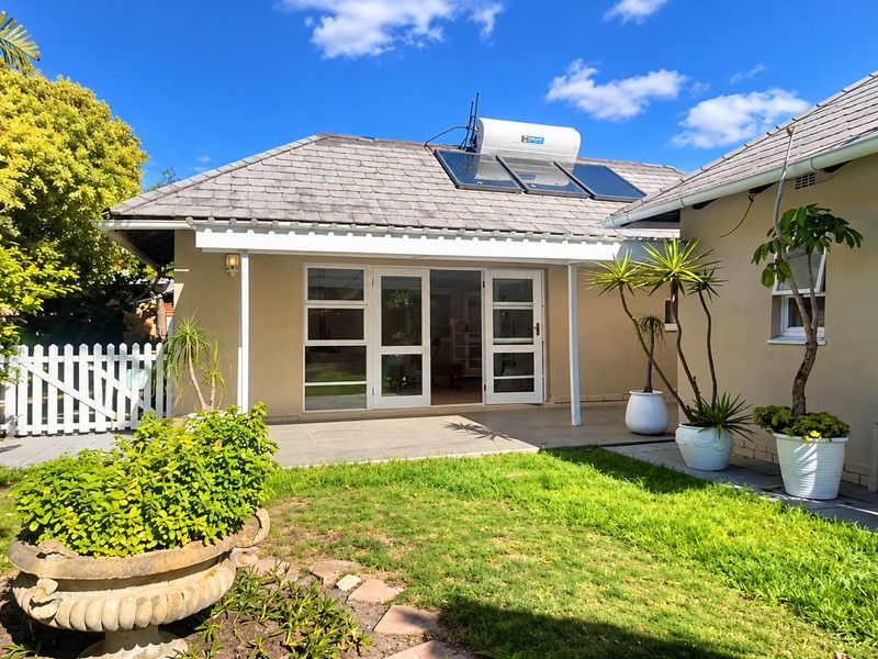 A well-maintained rear exterior view featuring a paved patio, lawn, white picket fence, and a roof-mounted solar water heating system.