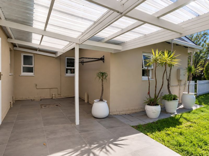 A covered patio area featuring tiled flooring and a translucent roof, providing a functional outdoor space adjacent to the garden.