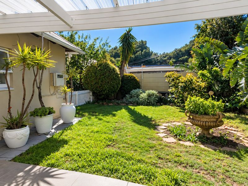 A well-maintained covered patio area featuring tiled flooring and a timber pergola, overlooking a private garden with established landscaping and boundary fencing.