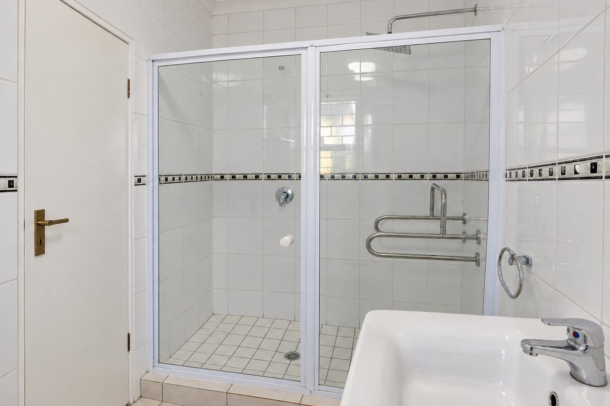 A clean, functional bathroom featuring a walk-in shower with grab rails, white wall tiling with decorative border, and a modern basin.