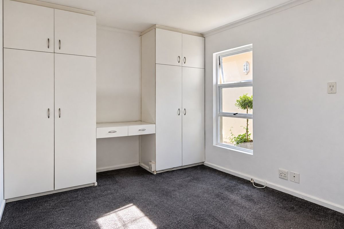 A bright, empty bedroom featuring neutral walls, dark carpeting, and ample built-in storage with an integrated desk area.