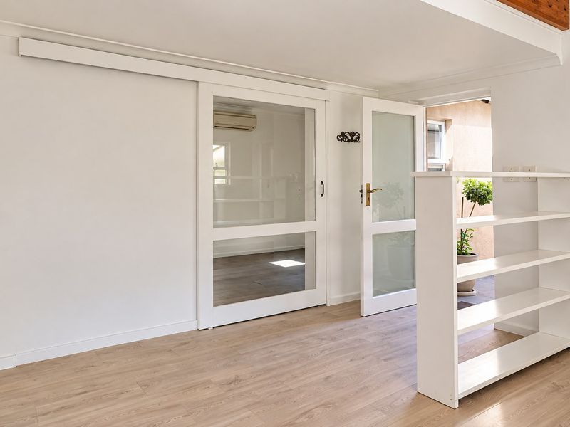 Bright and airy living space featuring modern laminate flooring, a sliding glass door, and a built-in shelving unit, offering a clean and versatile layout.