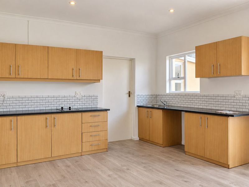 A clean, modern kitchen featuring light wood cabinetry, subway tile backsplash, dark laminate countertops, and durable wood-look flooring in an open, bright space.
