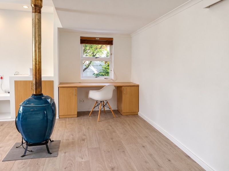A bright living area featuring a distinctive blue wood-burning stove, light wood-look laminate flooring, and a convenient built-in desk workspace.