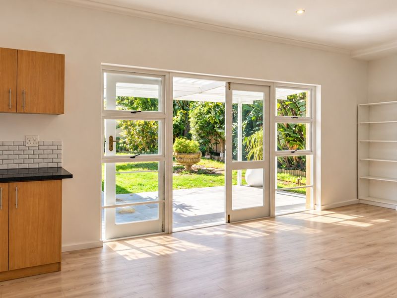 Bright open-plan living area featuring light wood-look flooring, built-in cabinetry, and large sliding glass doors providing seamless access to the rear patio and garden.