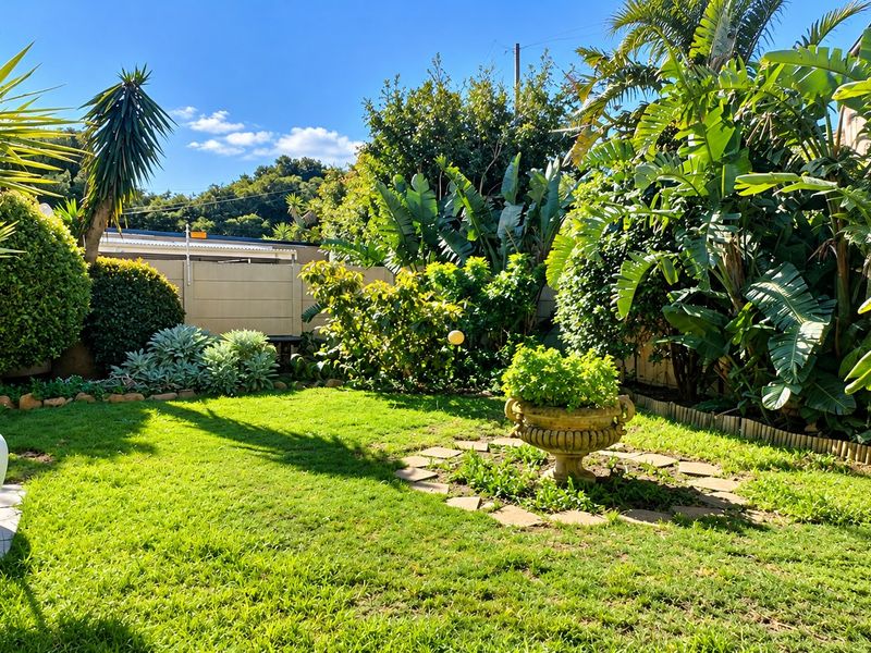 A well-maintained private garden featuring a lush lawn, mature tropical landscaping, and a decorative stone garden feature.