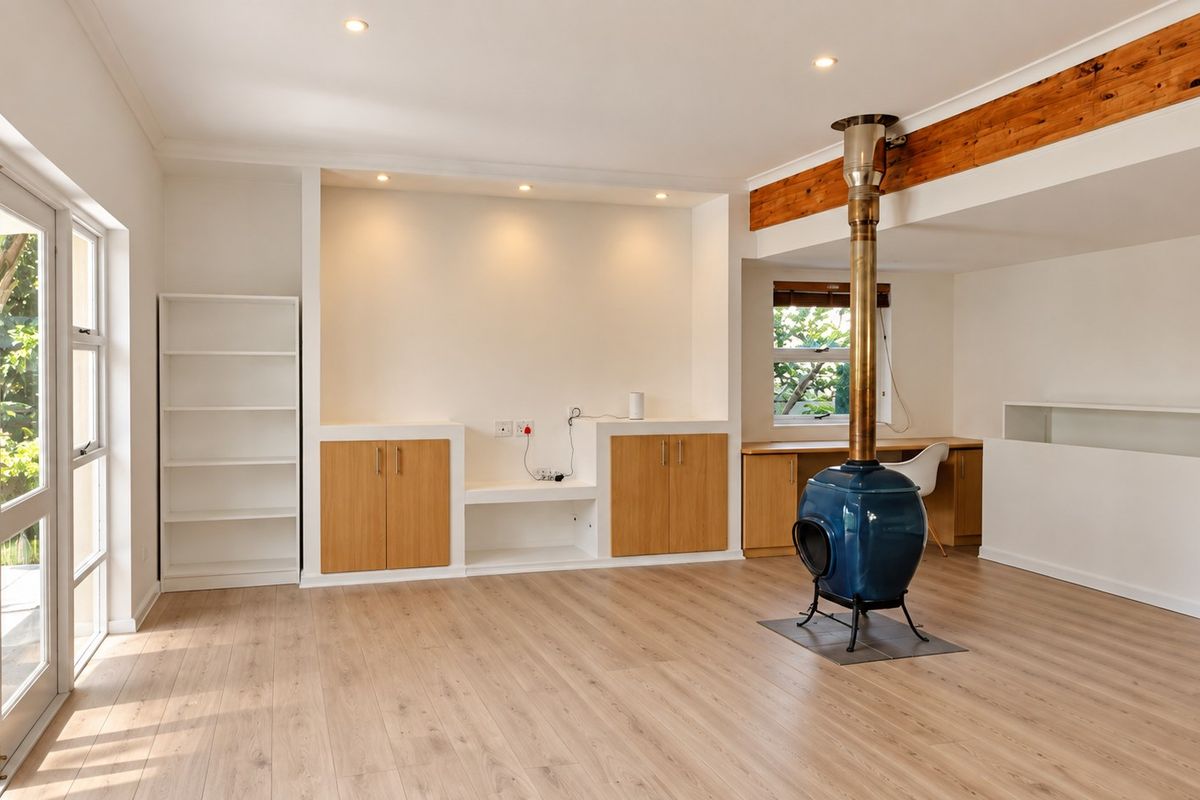 Spacious living area featuring light laminate flooring, a unique freestanding fireplace, built-in cabinetry, and direct access to the garden through sliding glass doors.