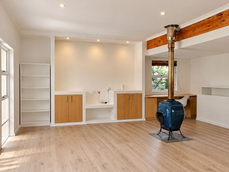 Spacious living area featuring light laminate flooring, a unique freestanding fireplace, built-in cabinetry, and direct access to the garden through sliding glass doors.