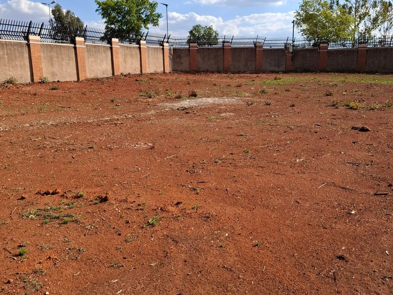 A vacant residential plot featuring a cleared earth surface enclosed by a perimeter wall with integrated brick pillars and security spikes.