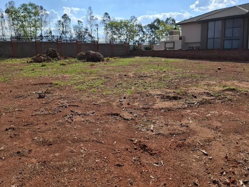 A vacant residential plot featuring red soil, perimeter walling, and security fencing, offering a blank canvas for future development.