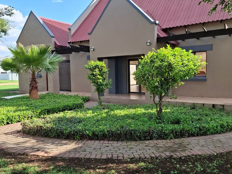 A well-maintained residential exterior featuring a distinctive red corrugated metal roof, a covered entrance, and a neatly landscaped garden with brick paving.