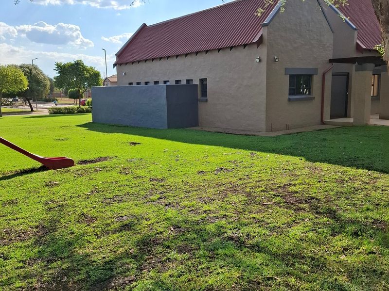 A view of the rear elevation of the residential building featuring a pitched metal roof, plastered exterior walls, and a well-maintained lawn area.