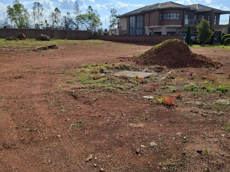 A vacant residential plot featuring cleared earth, a perimeter brick wall, and a central manhole cover, ready for development.