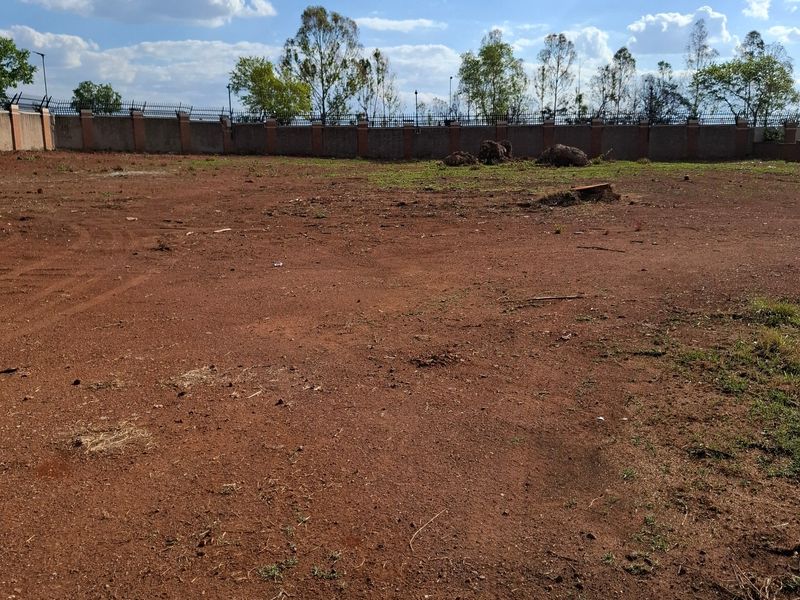 A vacant residential plot featuring cleared red earth and a secure perimeter wall with fencing along the boundary.