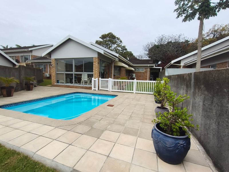 Private backyard featuring a swimming pool, paved patio area, and an enclosed sunroom, secured by boundary walls and a white picket fence.