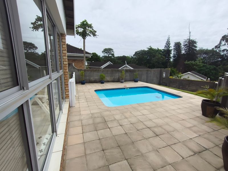 Outdoor pool area featuring a paved patio, swimming pool, and perimeter boundary wall, accessible via large aluminium sliding doors.