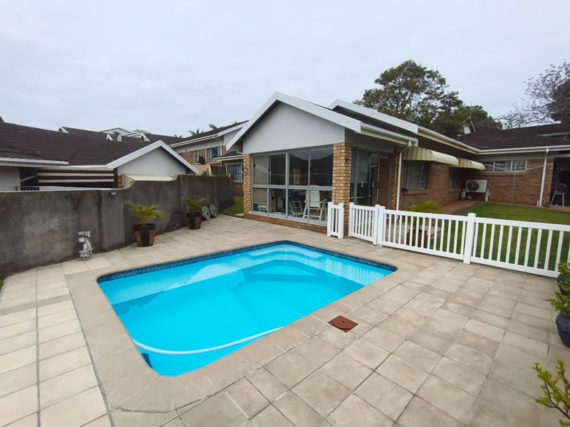 A private outdoor pool area featuring a paved patio, white picket fencing, and a brick-built townhouse exterior with aluminium window frames.