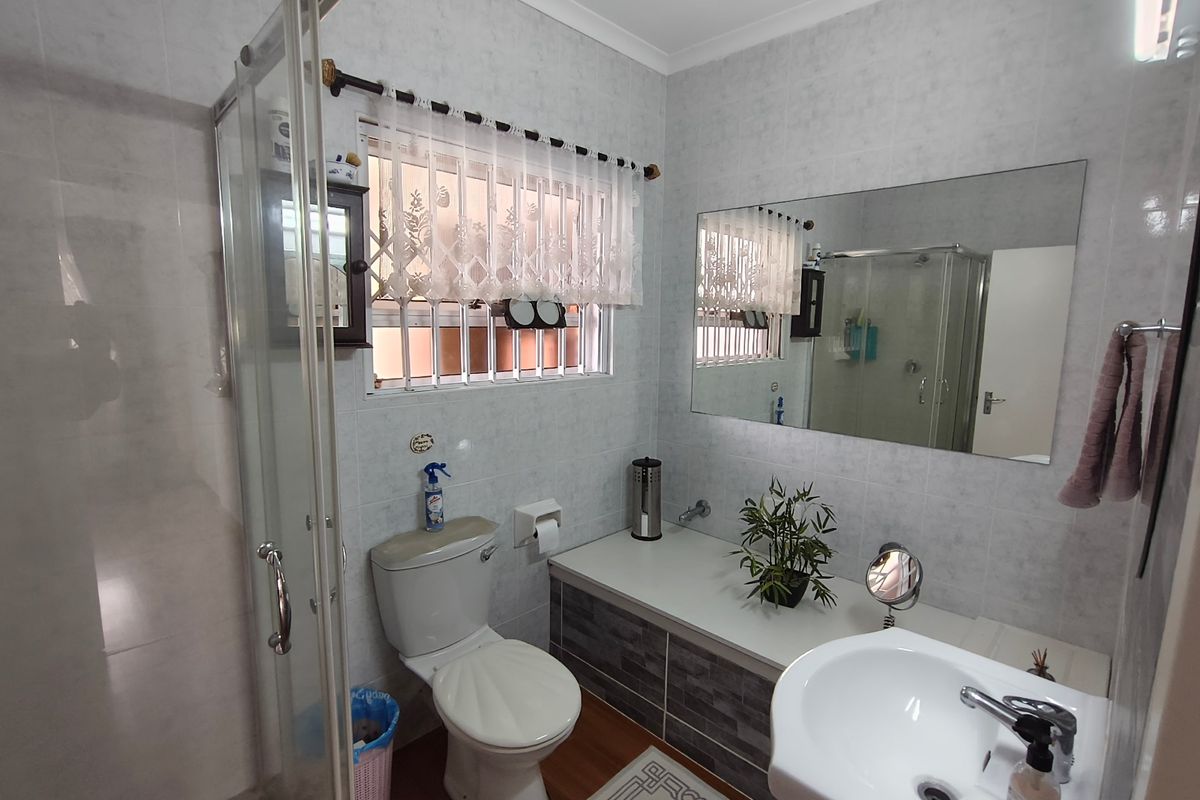 A functional bathroom featuring a shower enclosure, toilet, and vanity basin with wall-to-wall tiling and a large mirror.