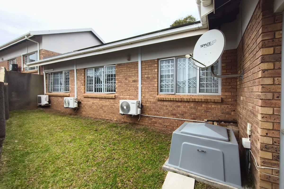 Rear exterior view of the townhouse featuring face brick walls, security window bars, multiple air conditioning units, and a dedicated generator enclosure.