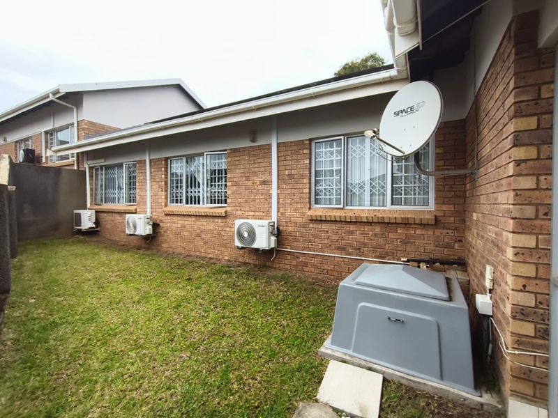 Rear exterior view of the townhouse featuring face brick walls, security window bars, multiple air conditioning units, and a dedicated generator enclosure.