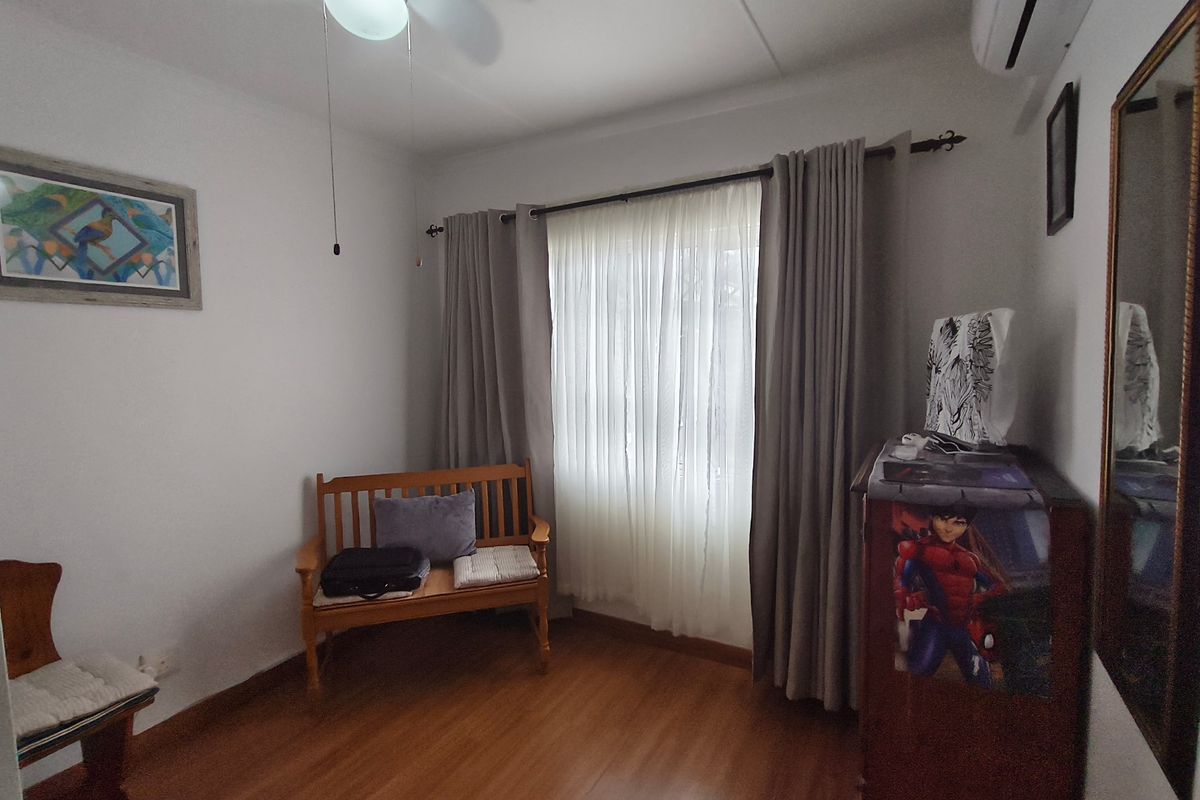 A bedroom featuring laminate flooring, a ceiling fan, and a wall-mounted air conditioning unit.