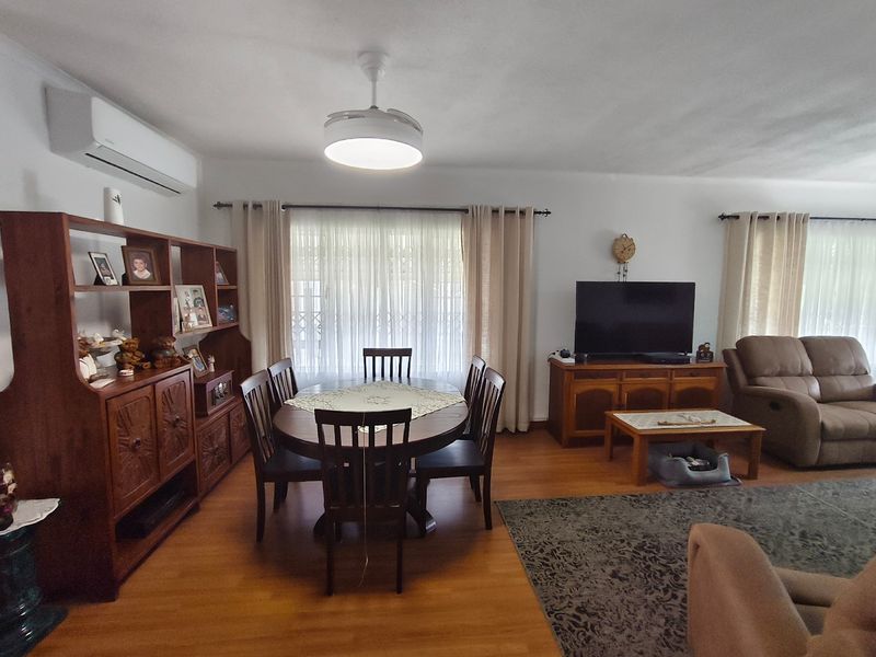 Spacious open-plan living and dining area featuring laminate flooring, a ceiling fan, and a wall-mounted split-system air conditioner.
