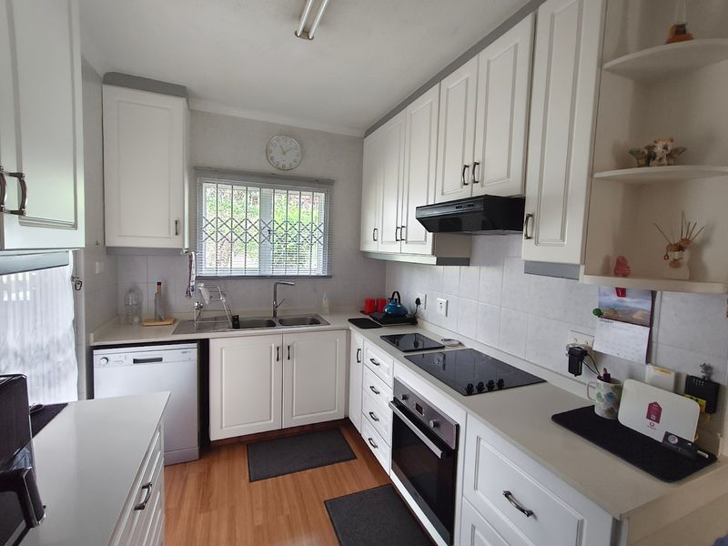 A functional kitchen featuring white cabinetry, integrated electric hob, oven, extractor fan, and a double sink with a security-fitted window.
