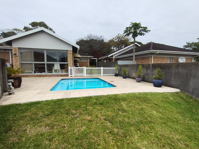 A private backyard featuring a swimming pool with a paved deck, enclosed by a boundary wall and a white picket fence.
