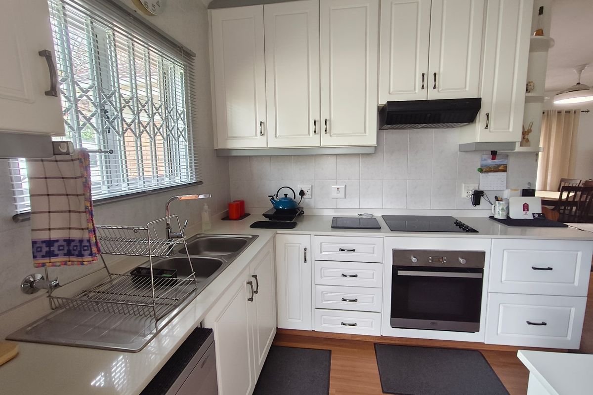 A well-maintained kitchen featuring white cabinetry, a double sink, built-in oven, electric hob, and a tiled backsplash with a window security gate.