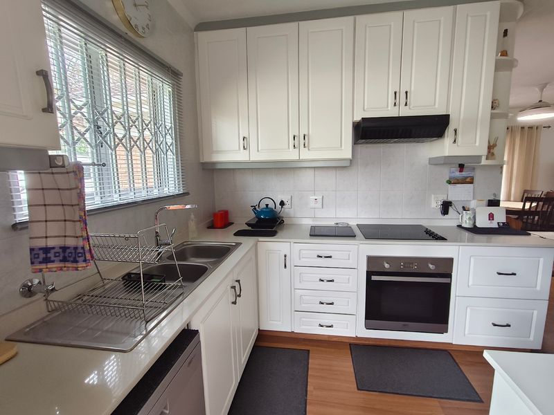 A well-maintained kitchen featuring white cabinetry, a double sink, built-in oven, electric hob, and a tiled backsplash with a window security gate.