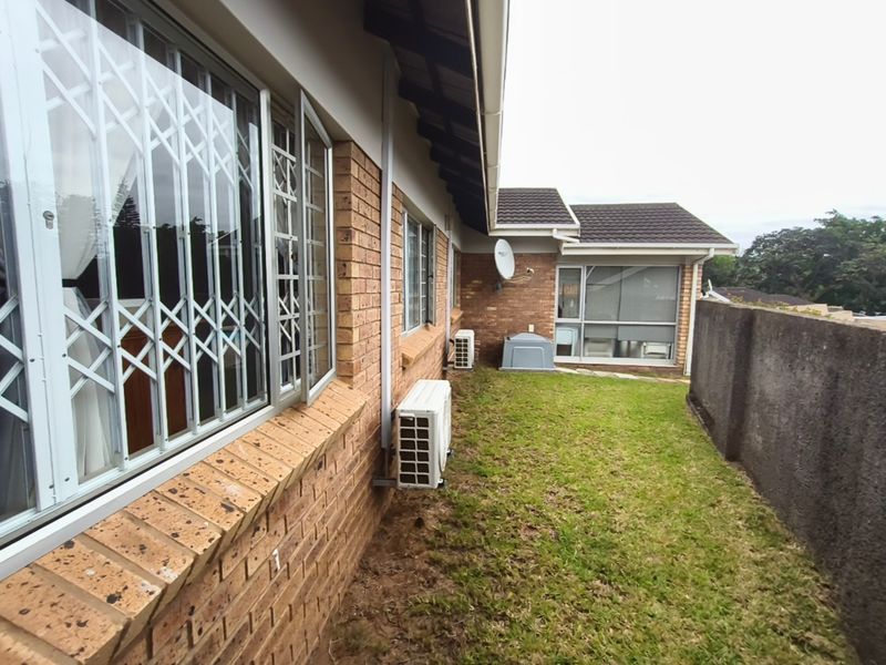 Rear exterior view of the townhouse featuring a face brick facade, security gates on windows, air conditioning units, and a private lawn area.