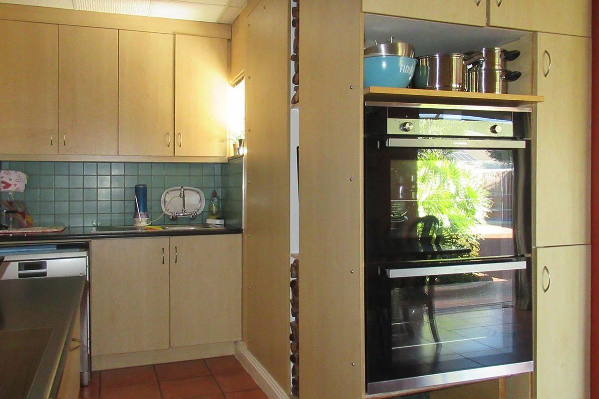 A functional kitchen featuring light wood-tone cabinetry, a double wall oven, tiled backsplash, and terracotta flooring, offering a practical layout for daily use.
