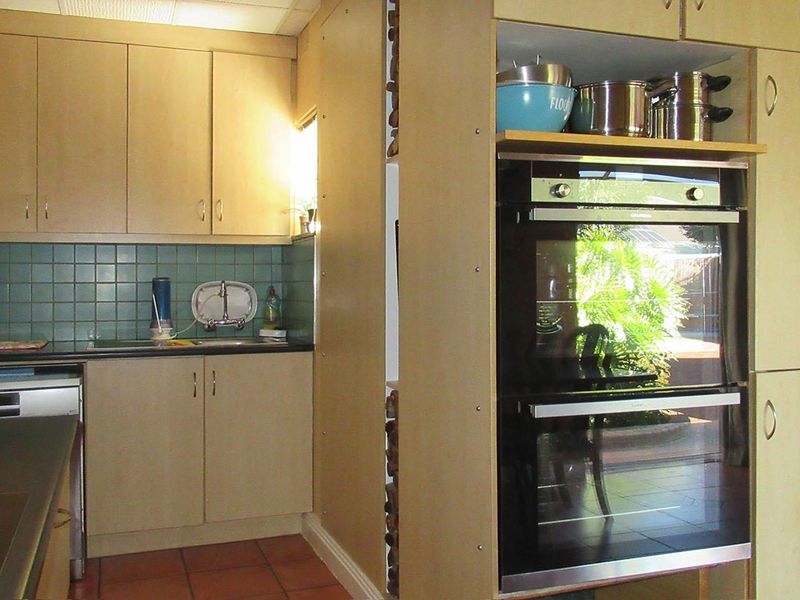 A functional kitchen featuring light wood-tone cabinetry, a double wall oven, tiled backsplash, and terracotta flooring, offering a practical layout for daily use.