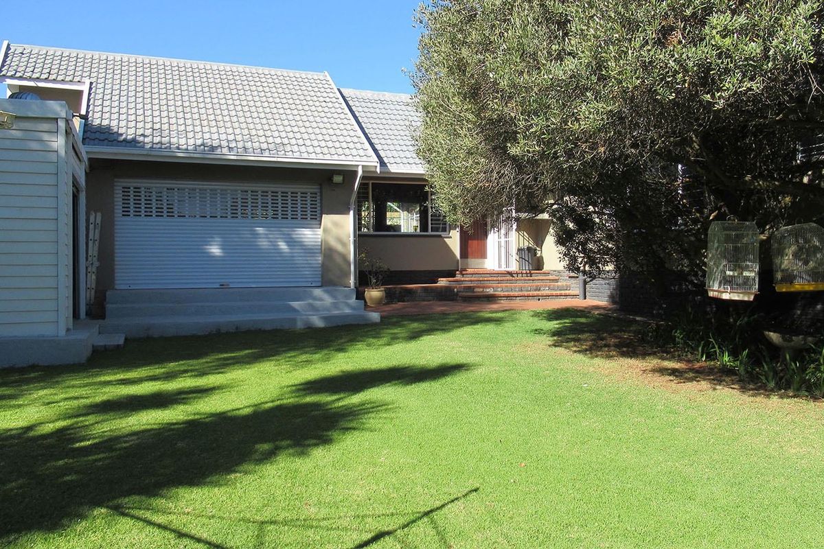 Rear view of the property featuring a well-maintained lawn, a brick patio area, and a garage with a secure roller shutter door.