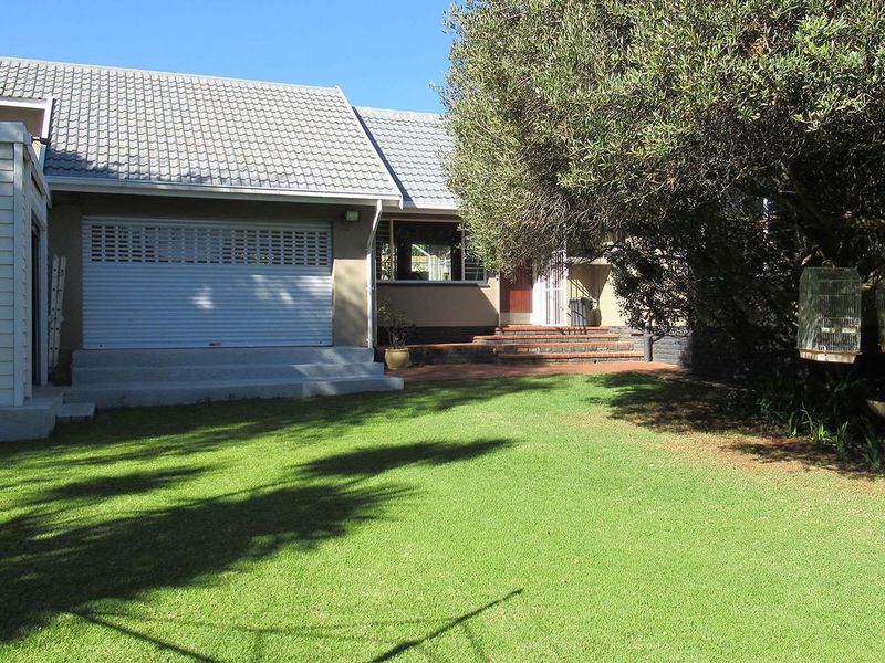 Rear view of the property featuring a well-maintained lawn, a brick patio area, and a garage with a secure roller shutter door.