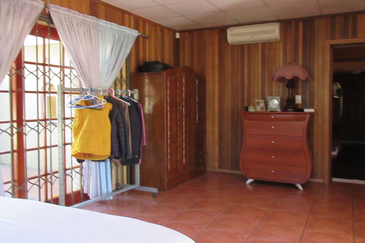 Bedroom featuring wood-paneled walls, tiled flooring, and a split-system air conditioner, with access to an outdoor area through security-gated french doors.