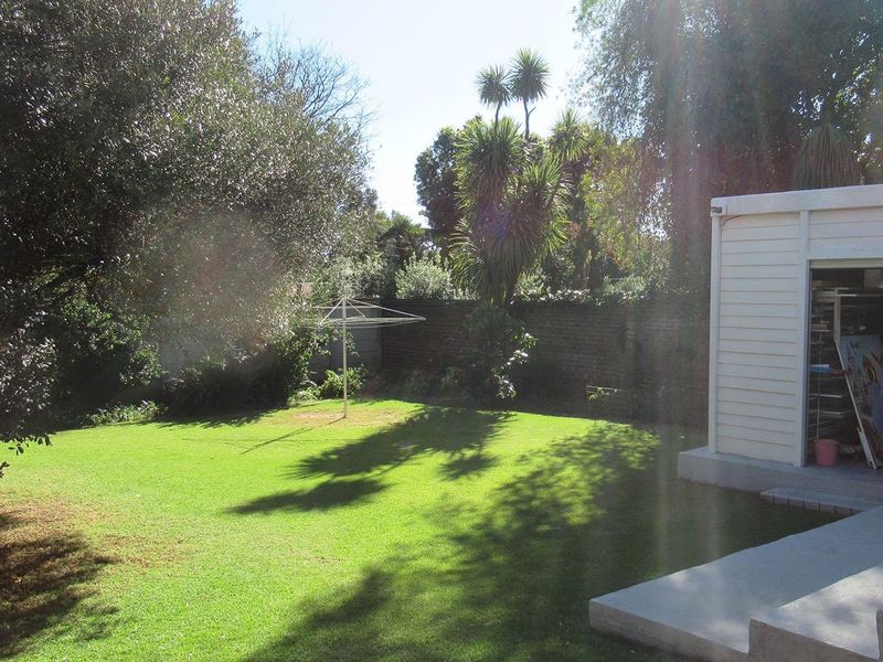 A spacious rear garden featuring a well-maintained lawn, brick boundary wall, and a detached garage structure with a concrete patio area.