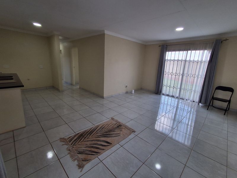 Spacious open-plan living area featuring neutral tiled flooring, recessed downlighting, and a sliding glass door with security gate leading to the exterior.