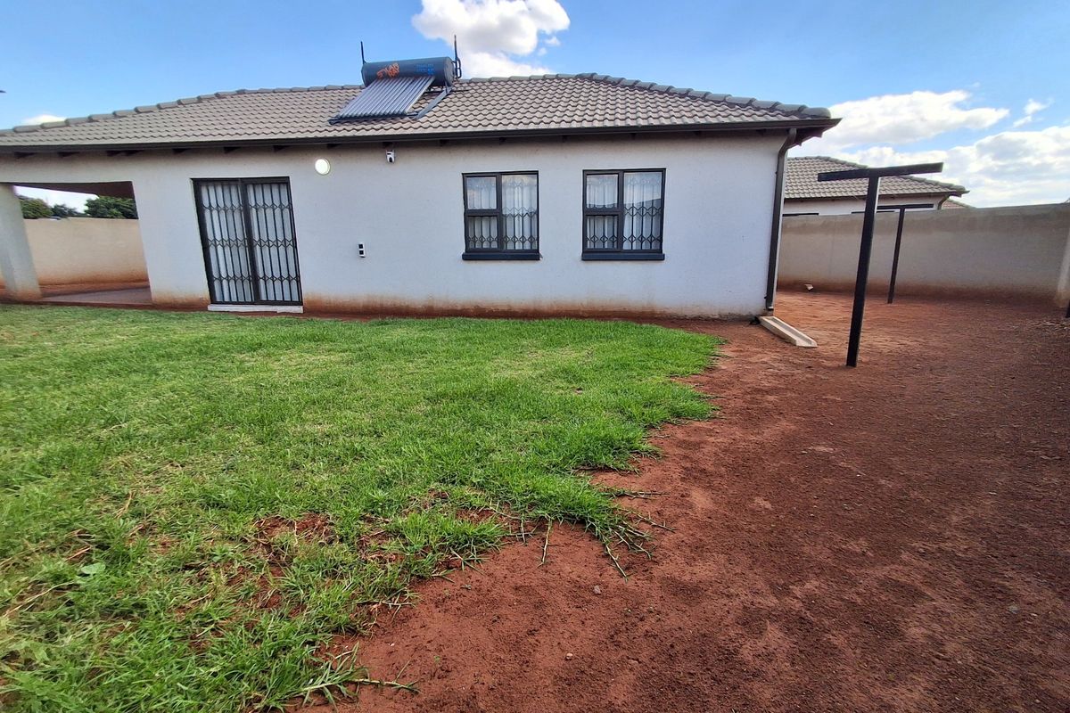 Rear view of the house featuring a solar water heater, security gates, and a spacious backyard with a lawn and washing line area.